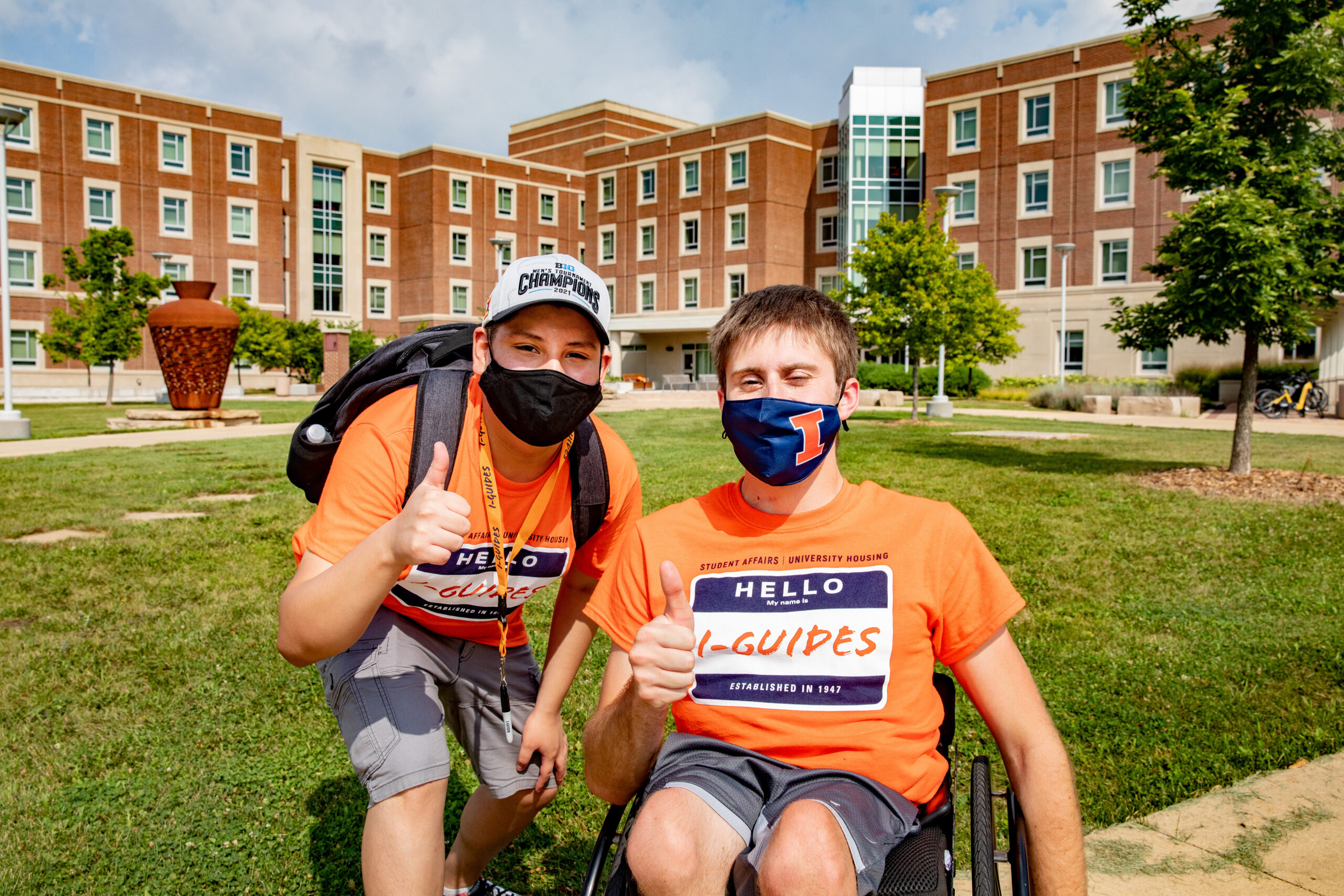 Two student I-guides, one in a wheelchair, posing for a photo in front of residence halls.